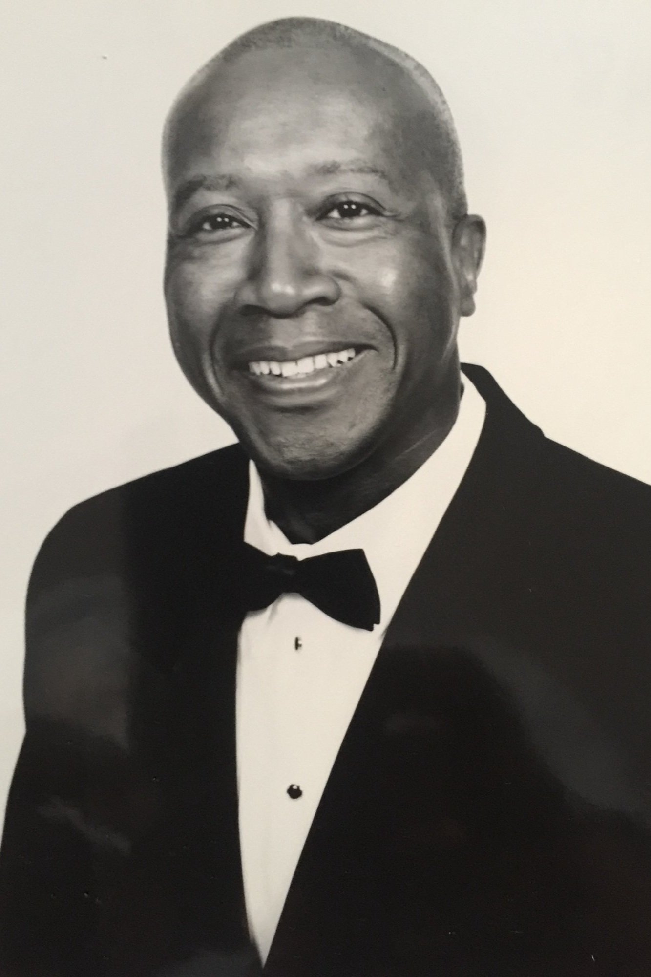 Man wearing a tuxedo and bow tie, smiling in a black and white portrait.