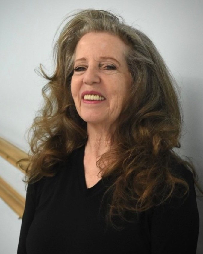 A smiling woman with long wavy hair wearing a black top against a neutral background.